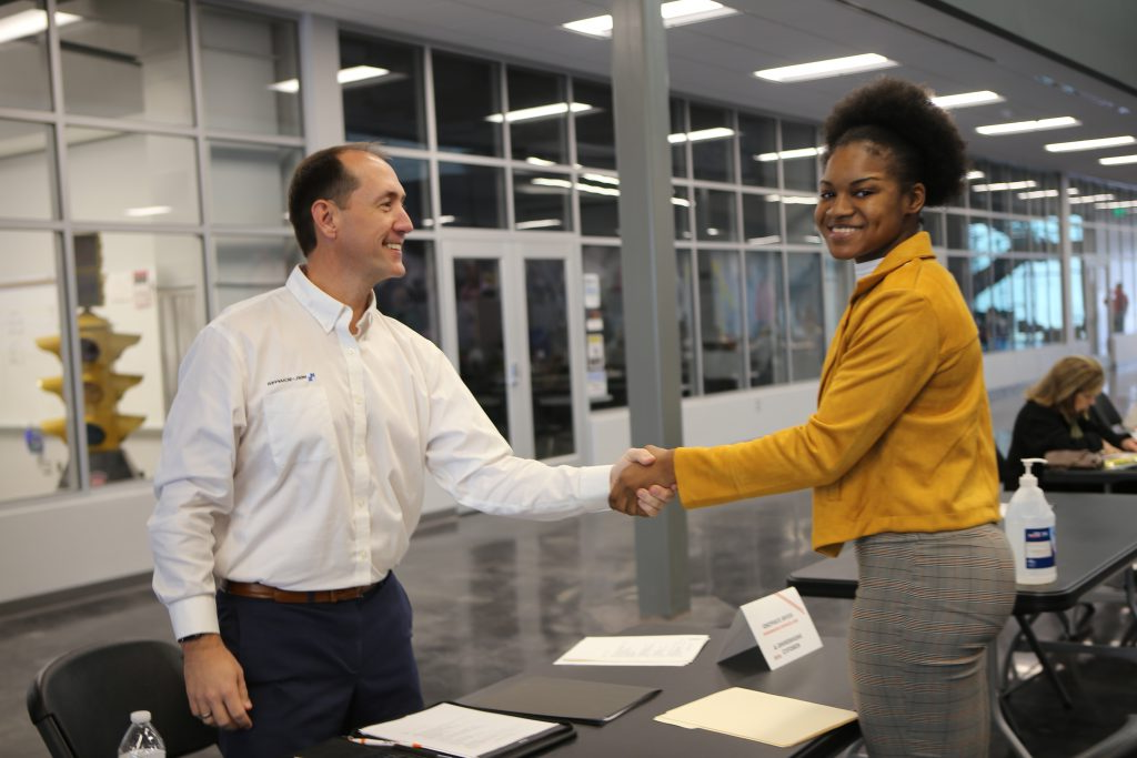 A young woman in a yellow collared shirt and grey slacks shakes hands with Kevin Stafford, city engineer.