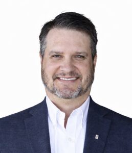 Headshot of Carey Edwards, smiling and wearing a navy blazer and white collared shirt.